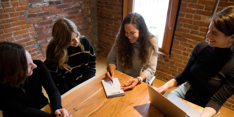 A group of 4 marketers sitting around a table with a laptop and pad of paper having a meeting